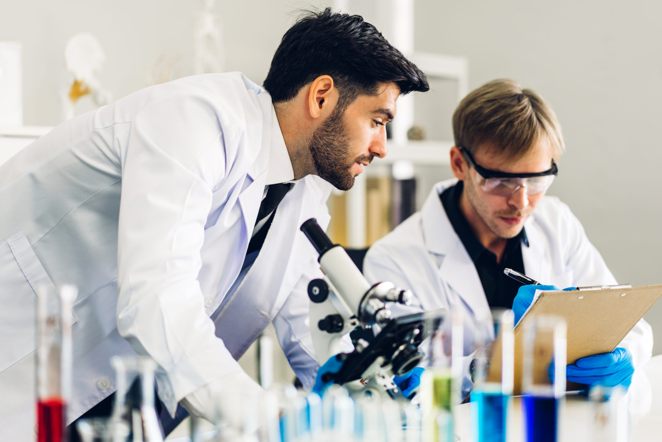 Professional two scientist man research and working doing a chemical experiment while making analyzing and mixing  liquid in test tube.Young science man dropping sample chemical on glass at laboratory